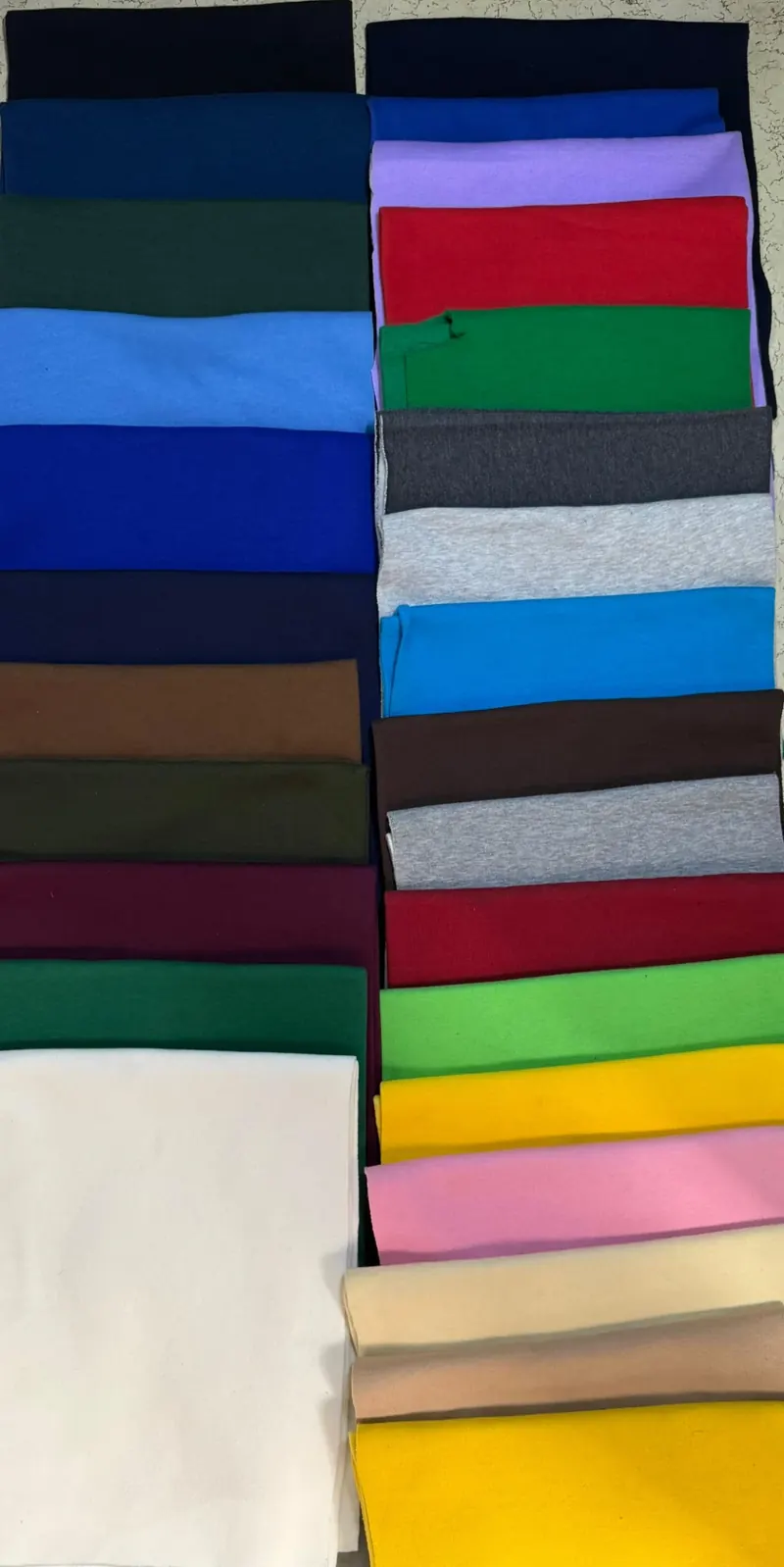 Folded sweatshirt fabric in navy, blue, green, red, yellow and pink, stacked in rows