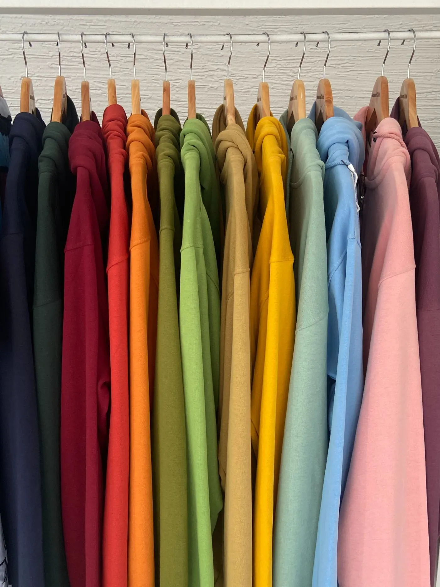 A row of plain sweatshirts in many colours hanging on wooden hangers